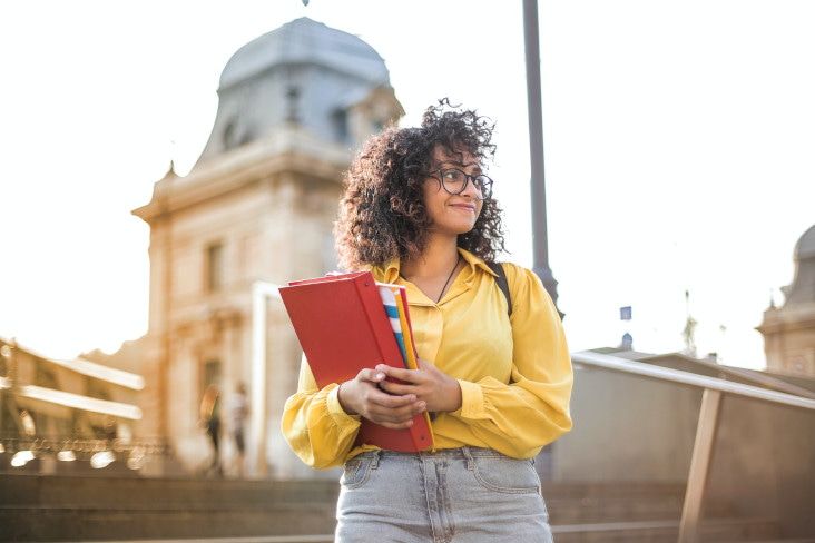 A girl holding her notes in her hand in the middle of the street smiles because she knows Todoist, one of the best apps for university students.